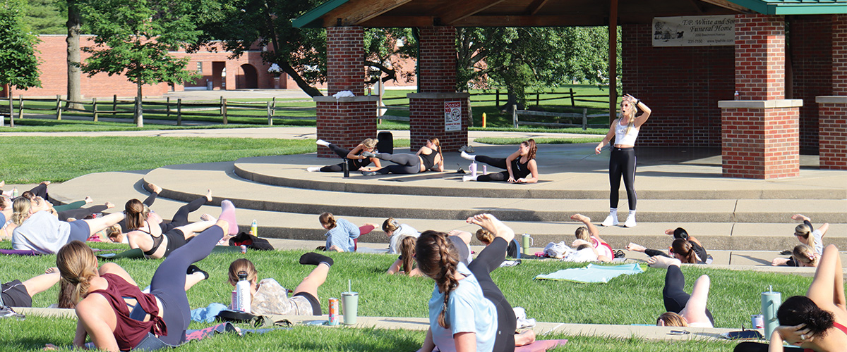 A group of woman laying on the ground performing pilates exercises at Beech Acres Park Amphitheater